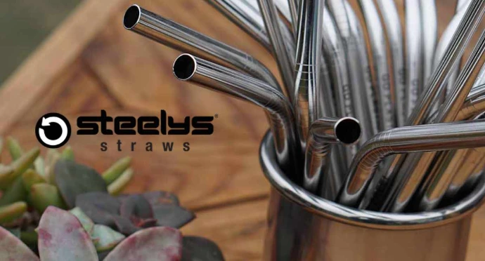 A collection of reusable stainless steel drinking straws in a metal container, featuring the Steelys Straws logo and green succulent plants in the foreground.